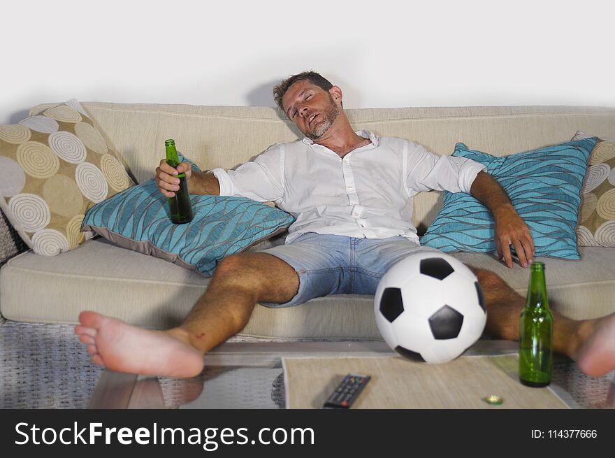 Young wasted soccer supporter man lying on home sofa couch sleep
