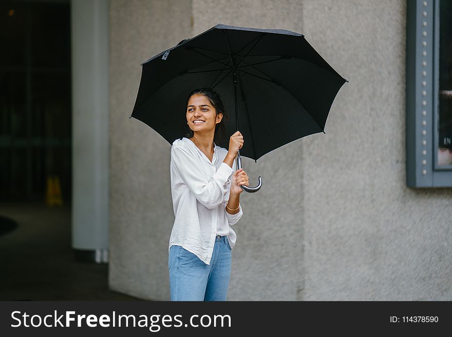 Photo Of Woman Wearing White Long-sleeved Shirt And Blue Jeans Holding Black Umbrella