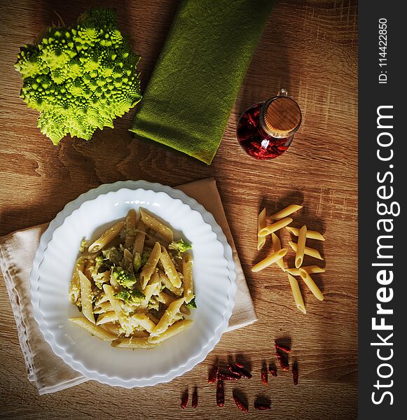 Pasta and roman cauliflower on a wooden table surrounded by raw ingredients