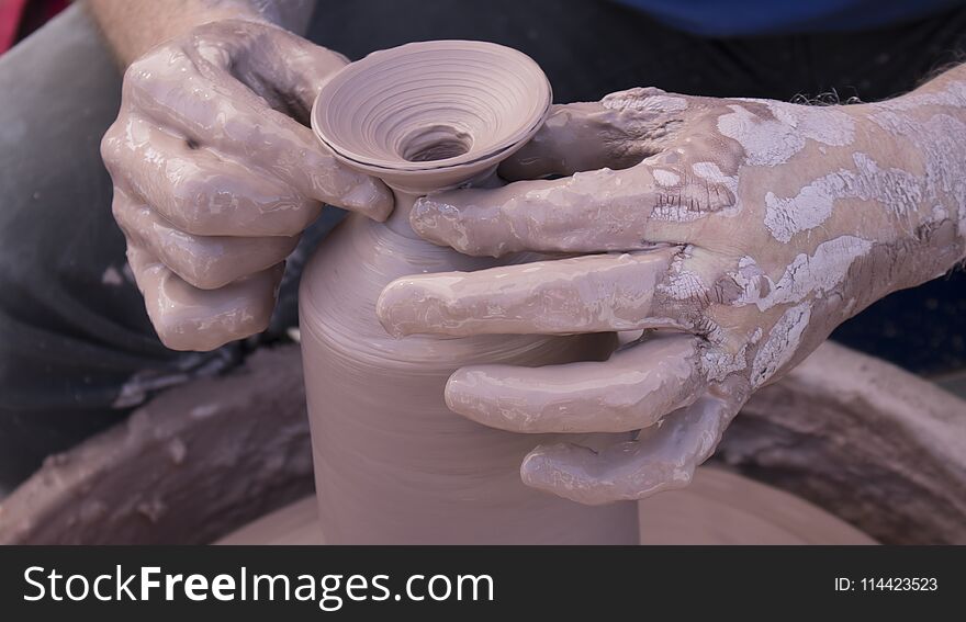 A Potters hands covered in clay forming a pot on a wheel close up