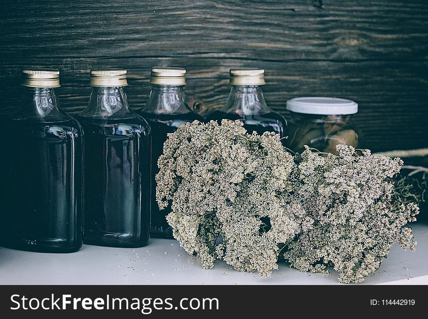 Four Clear Glass Bottles With Black Liquid Near Brown Flower Bouquet