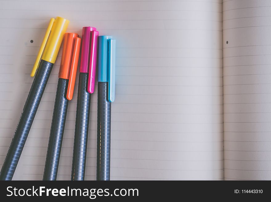 Yellow, Orange, Pink, and Blue Coloring Pens on White Notebook