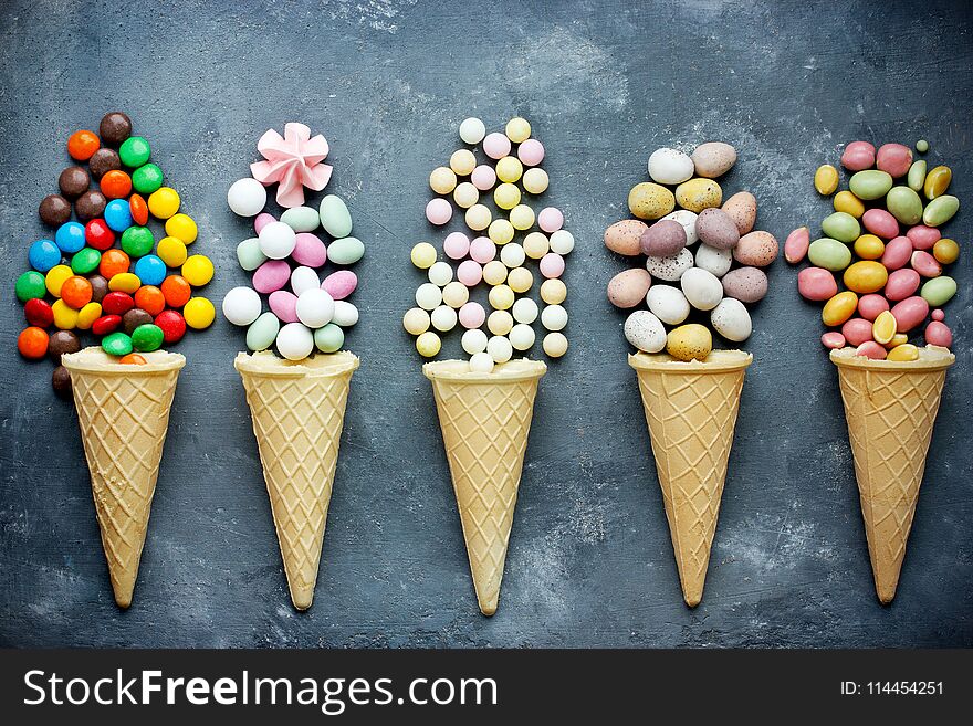 Candy in waffle cones on dark background. Flat lay, top view