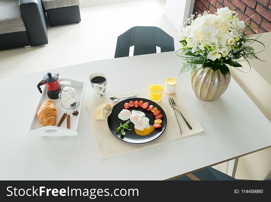 Breakfast with poached eggs and tomatoes, croissant, juce and cup of coffee served on dinner table