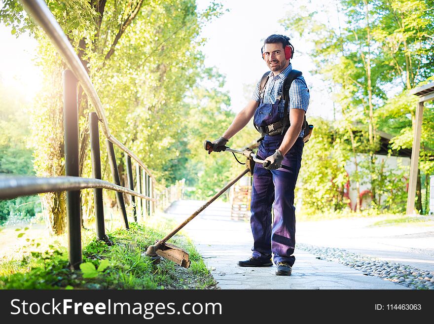 Man wearing ear protectors mowing grass in the backyard with petrol hedge trimmer. Man wearing ear protectors mowing grass in the backyard with petrol hedge trimmer