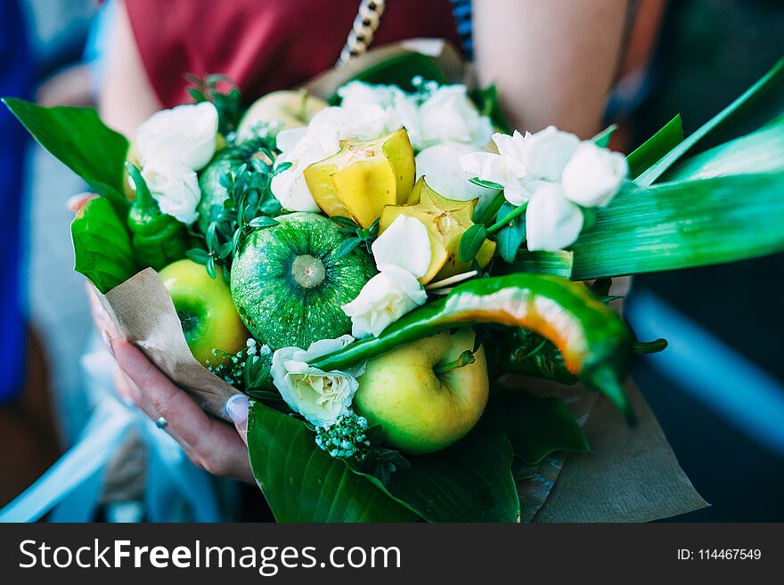 Fragment of original unusual edible bouquet of vegetables and fruits. Green apples, carrots, zucchini, dark green pepper, purple onion, decorative cabbage. Close up. Selective focus.