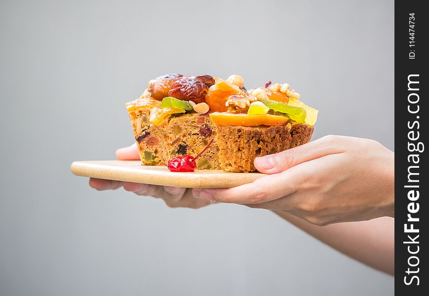 Female hand holding a loaf of fruit cake on wooden plate