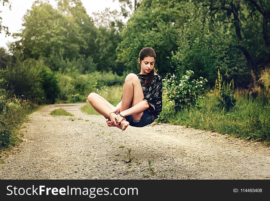 Beautiful stylish hipster girl levitating with peaceful feelings on the road near woods in summer