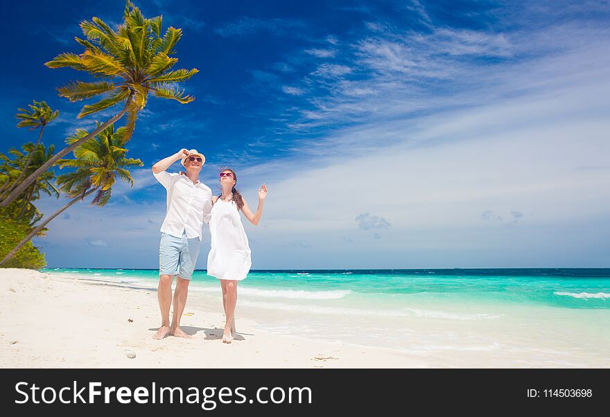 Happy young couple in white clothes walking by the beach. Maldives