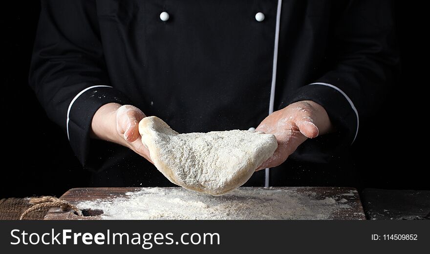 Female chef holding yeast dough in her hands on black background