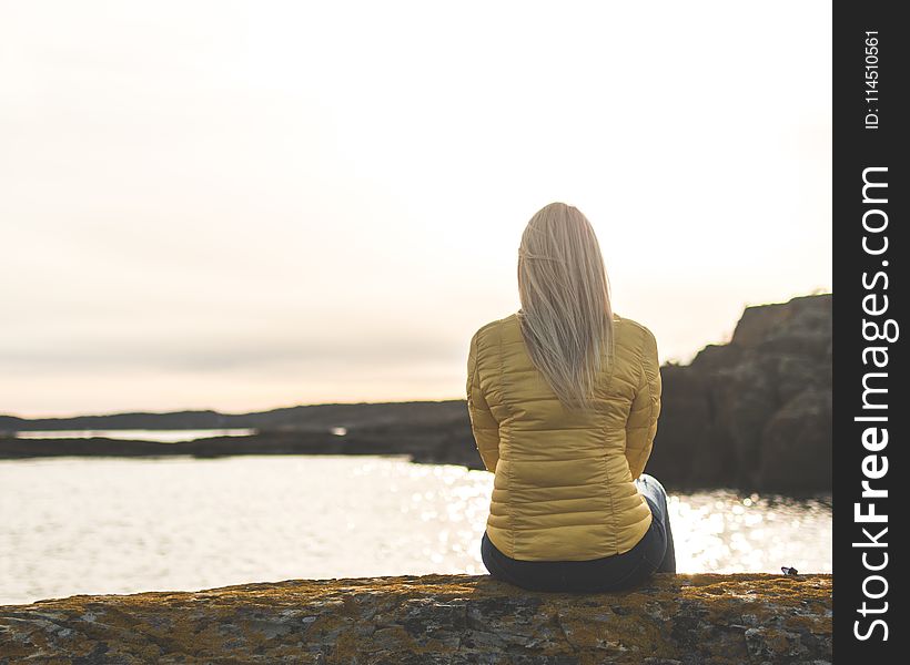 Woman Wearing Yellow Bubble Jacket Sitting In Front Of Sea