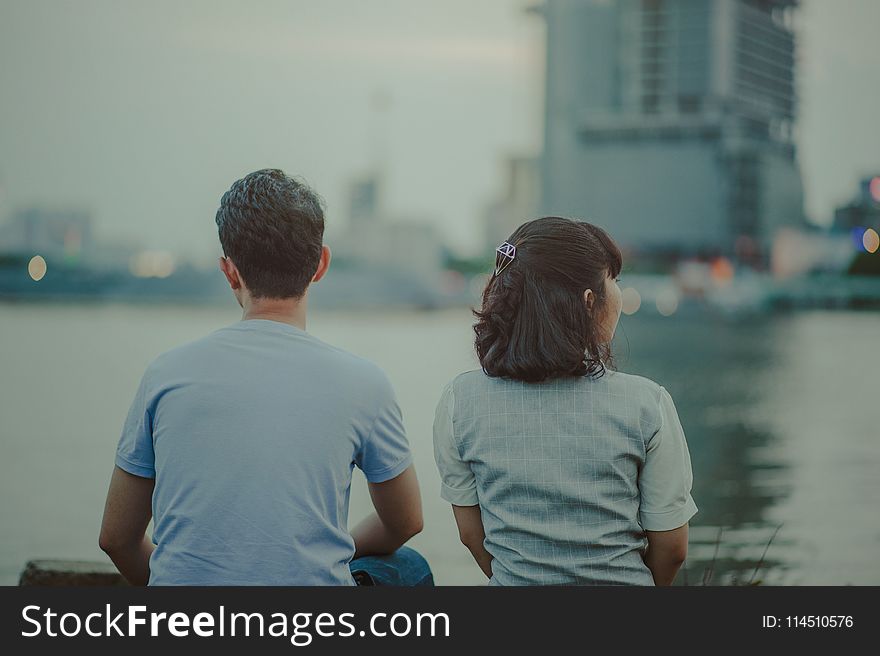 Selective Focus Photography of Man and Woman Watching Body of Water and Concrete Buildings