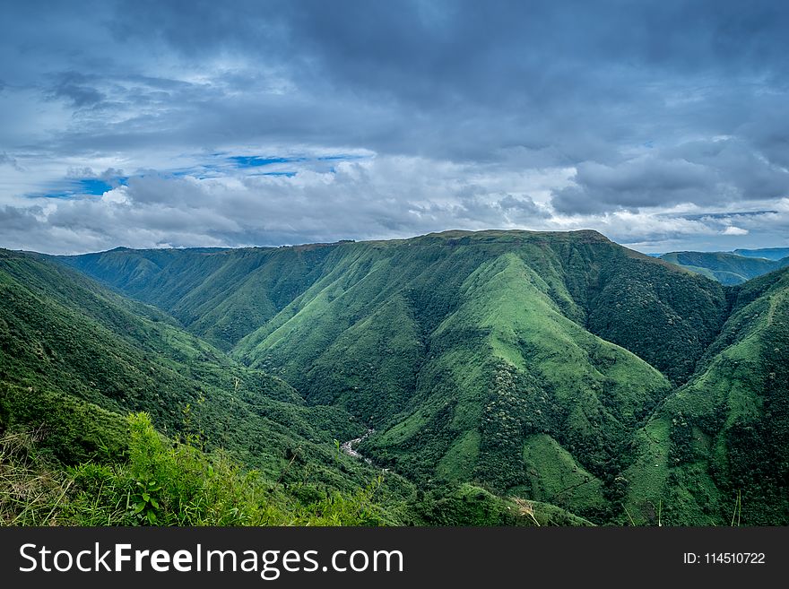 Landscape Photography Of Green Mountains Under Cloudy Sky