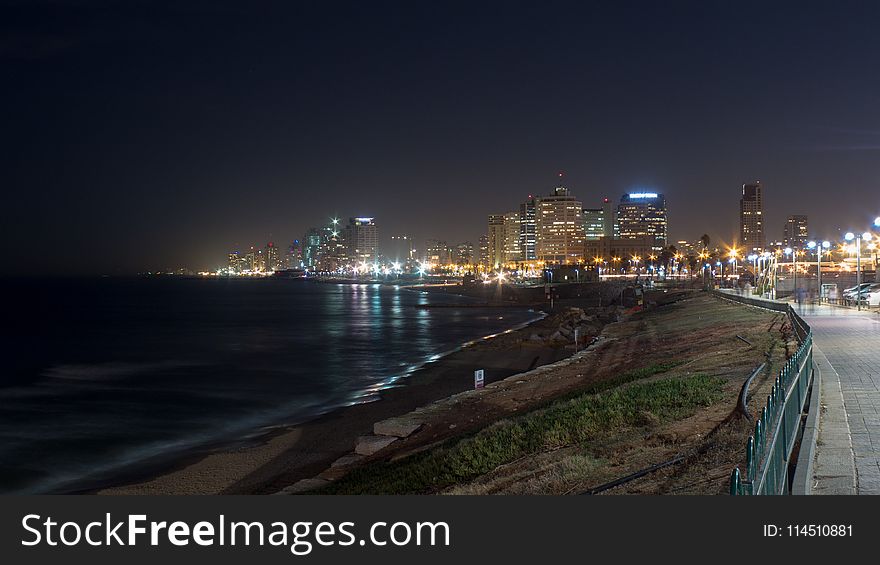 Grey Concrete Way Near Body of Water Leading to City during Nighttime