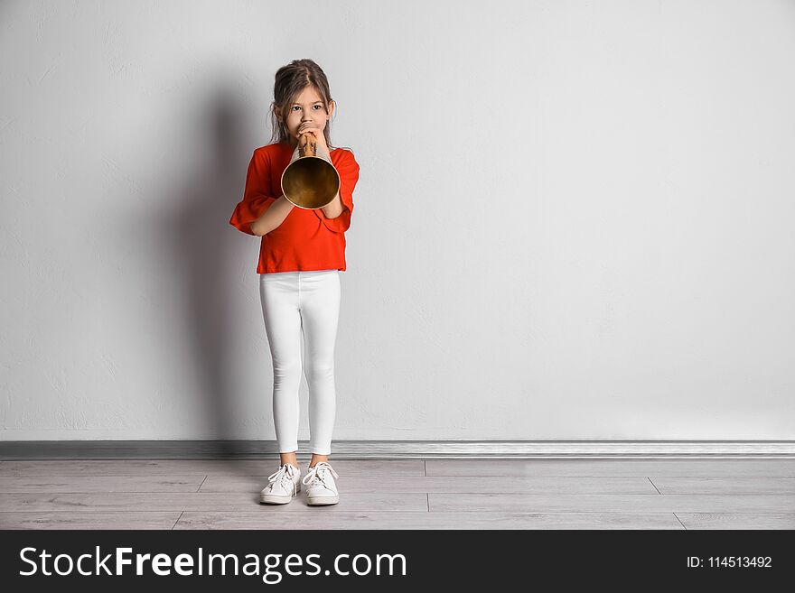 Adorable little girl with vintage megaphone near wall