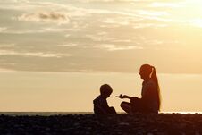 Mom And Son Playing On The Beach With Stones. Sunset Time, Silhouettes Stock Image