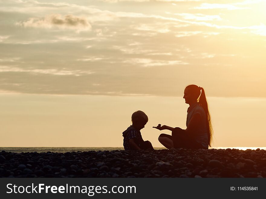 Mom and son playing on the beach with stones. Sunset time, silhouettes.