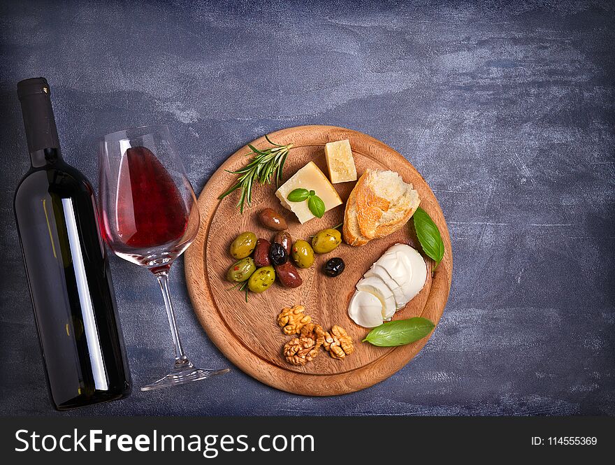 Bottle and glass of wine with cheese, olives, bread, nuts and basil on dark background.