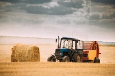 Tractor Collects Dry Grass In Straw Bales In Summer Wheat Field. Royalty Free Stock Photos