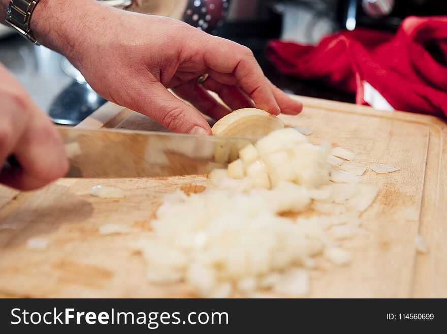 Close up shot of a mature man cutting up an onion on a chopping board inthe kitchen of his home. Close up shot of a mature man cutting up an onion on a chopping board inthe kitchen of his home.