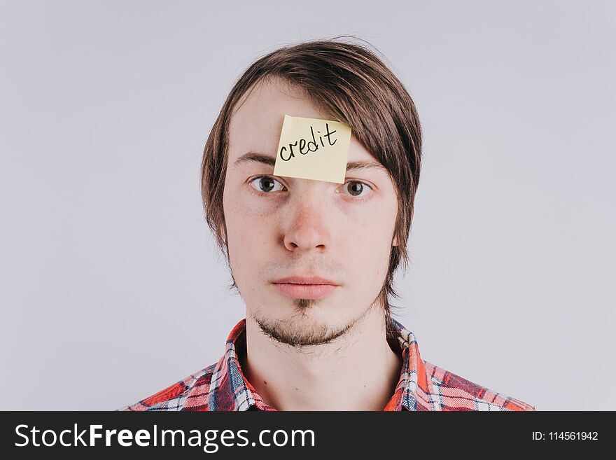 Sad man looks directly, the sticker is glued on the forehead with the word credit . A young guy is upset by debt, credit