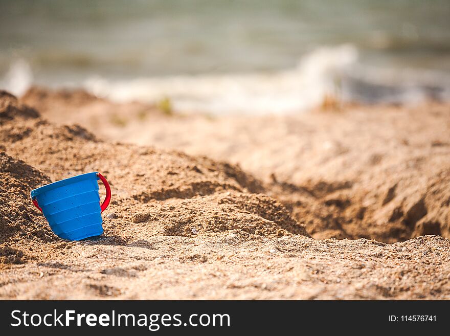 A plastic pail in the sand. Baby bucket seashore. Working tool against the background of the sea coast. Children`s plastic bucket.