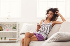 Young Thoughtful Girl Using Mobile Phone On Sofa Stock Image