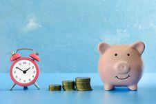 On A Dark Blue Background Photographed Piggy Bank, Next To Her A Small Pink Alarm Clock And Three Stacks Of Coins Royalty Free Stock Photo