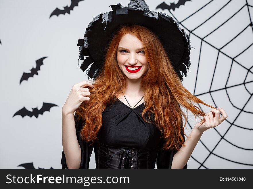 Halloween witch concept - Happy Halloween Witch holding posing over dark grey studio background with bat and spider web.