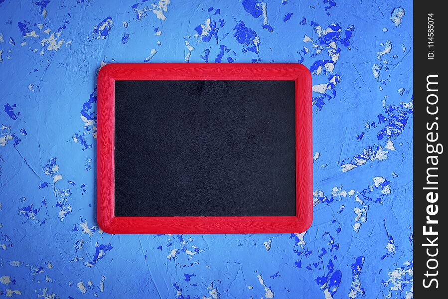 Empty black chalk board in a red frame on a worn blue surface, close up