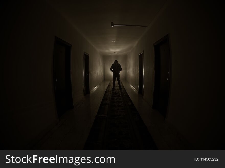 Creepy silhouette in the dark abandoned building. Dark corridor with cabinet doors and lights with silhouette of spooky horror per