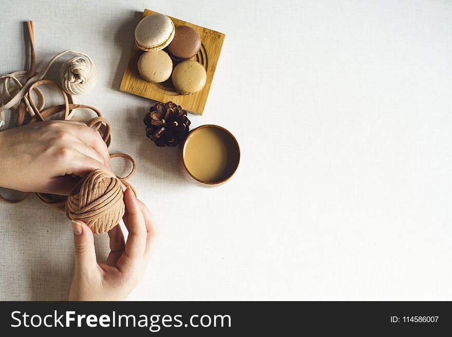 Homemade colorful macarons on the wooden plate on the white background. Female hand is holding yarn. Flat lay with copy space for text. Homemade colorful macarons on the wooden plate on the white background. Female hand is holding yarn. Flat lay with copy space for text