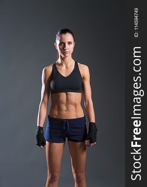 Muscular young woman posing in sportswear against black background.