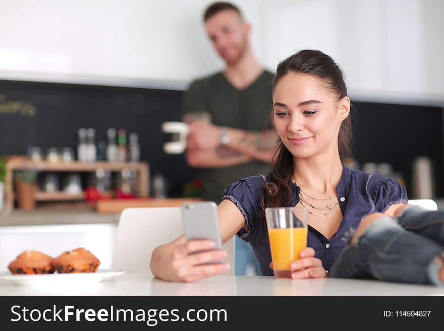 Happy couple using smartphone sitting in kitchen