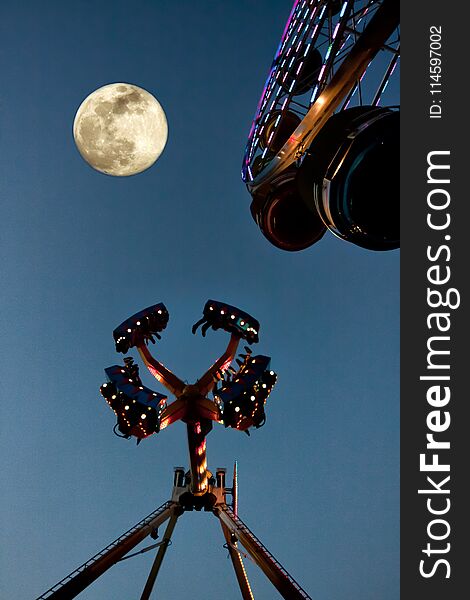 Fair rides at a fair at night with the moon. Fair rides at a fair at night with the moon