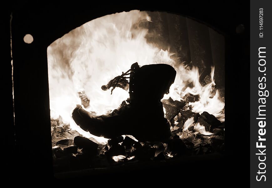 Old army boots burning in the furnace of the flame to hug the wall of fire the contour of the boot. Old army boots burning in the furnace of the flame to hug the wall of fire the contour of the boot