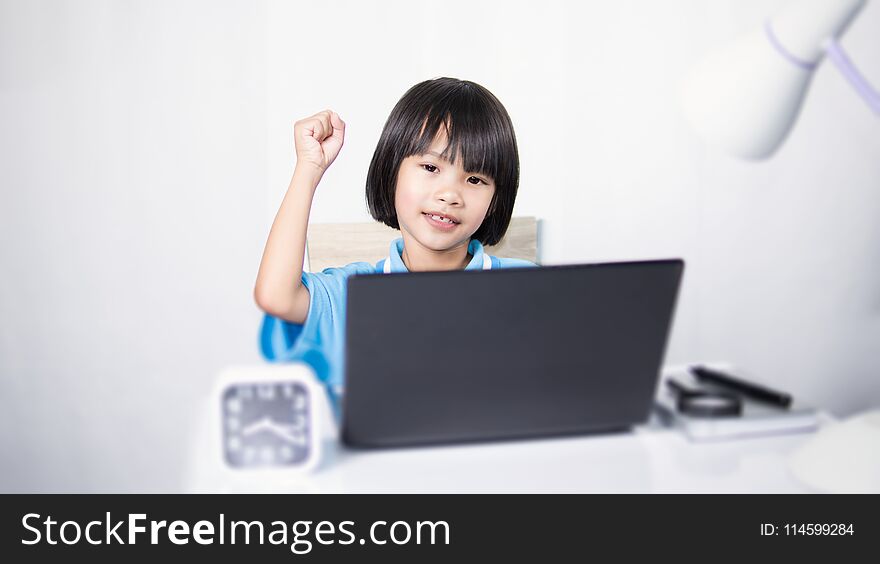 Cute child thinking and typing laptop. Asian child girl working on work desk. She sitting on chair on white gray fabric background.