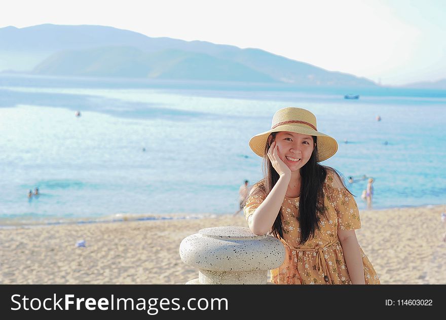 Woman Wearing Yellow Floral Dress And Sun Hat On Beach