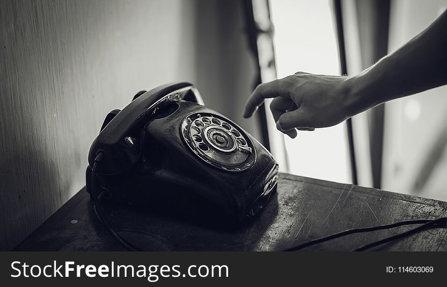 Grayscale Photo of Rotary Telephone Beside Person Hand