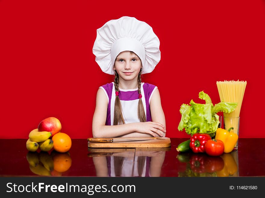 Happy little girl in chef uniform cuts fruit in kitchen. Kid chef. Cooking Process Concept