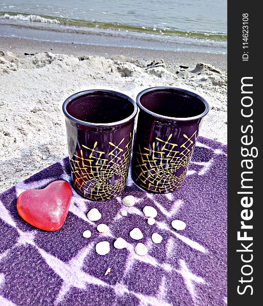 On the beach there are two cups and a heart