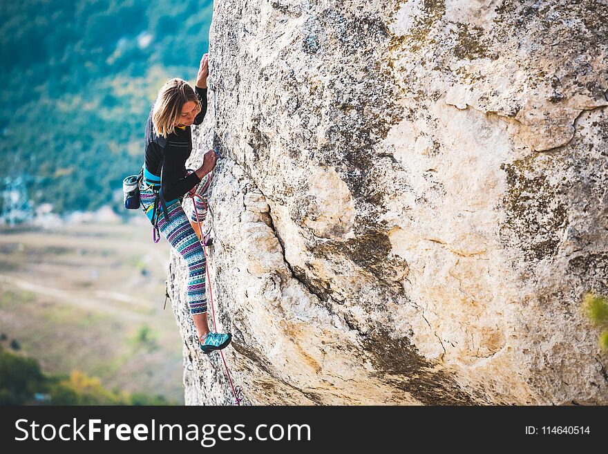 The girl climbs the rock. The climber trains on a natural relief. Extreme sport. Active recreation in nature. A woman overcomes a difficult climbing route.