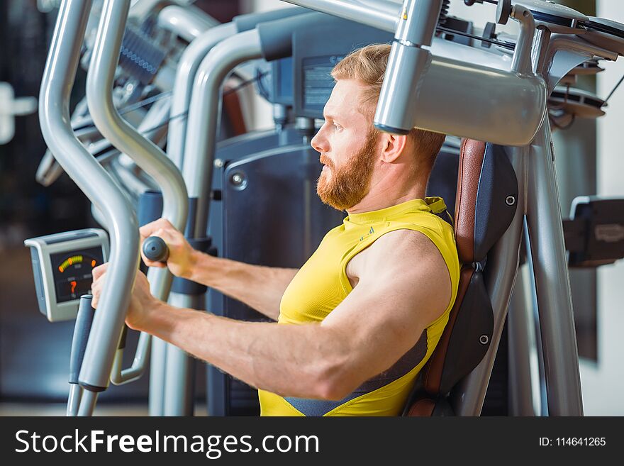 Portrait of a handsome bodybuilder smiling and looking at camera while exercising at a modern fitness machine for pectoral fly and deltoid workout