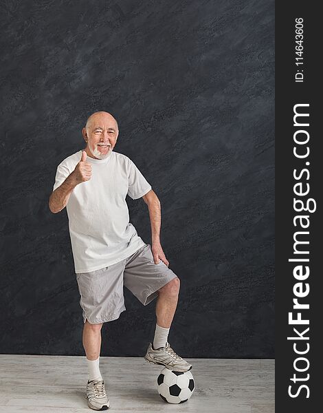 Smiling senior man posing with soccer ball showing thumb up gesture, black background. Hobby, active lifestyle in any age and motivation, copy space. Smiling senior man posing with soccer ball showing thumb up gesture, black background. Hobby, active lifestyle in any age and motivation, copy space