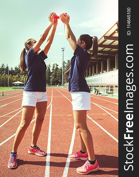 Two young and beautiful female athletes lifting as a joke a heavy dumbbell. Two young and beautiful female athletes lifting as a joke a heavy dumbbell