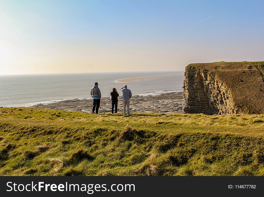 Three People On Top Of Hill Near Body Of Water