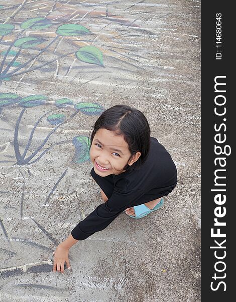 A little girl with a smile sitting on a painted cement background