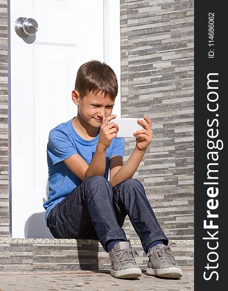 Boy With Mobile Phone Sitting On Staircase In Front Of A Door