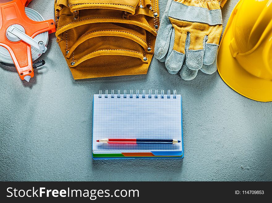 Protective gloves hard hat notepad pencil tool belt tape measure on concrete background.