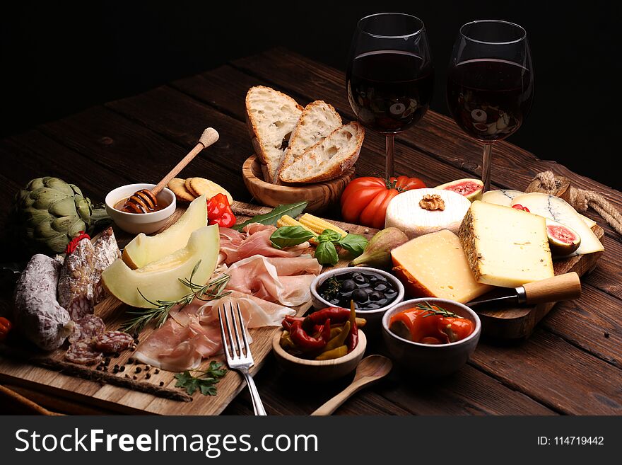 Italian antipasti wine snacks set. Cheese variety, Mediterranean olives, pickles, Prosciutto di Parma with melon, salami and wine in glasses over black grunge background